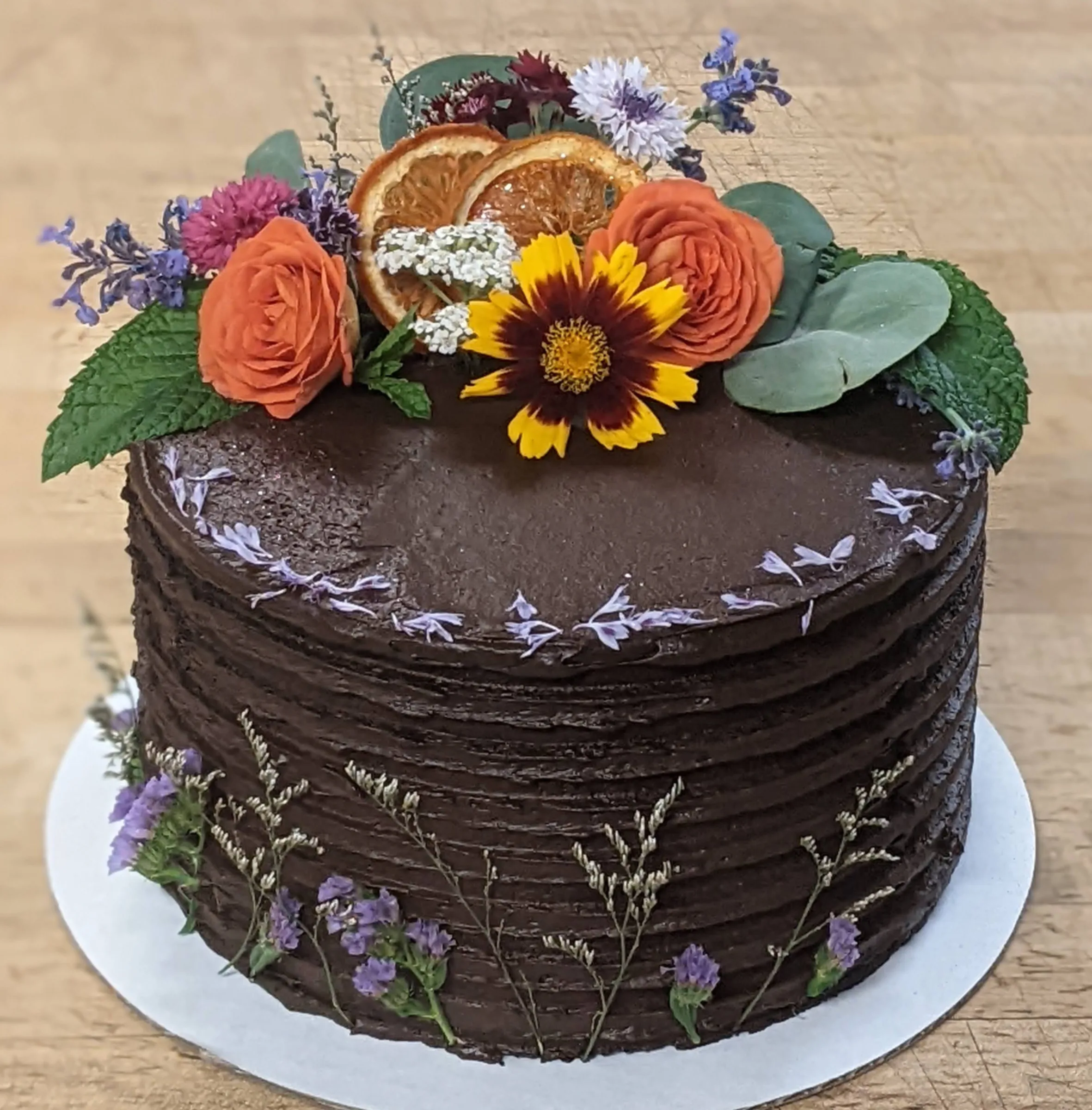 Chocolate buttercream cake topped with dried orange slices, orange roses, coreopsis and mint, with dried statice pressed into the side