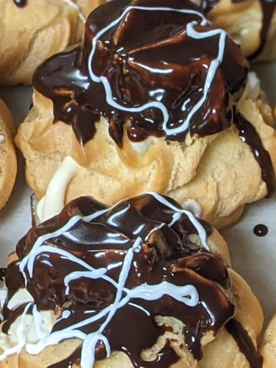 Cream puffs topped with chocolate and a white drizzle