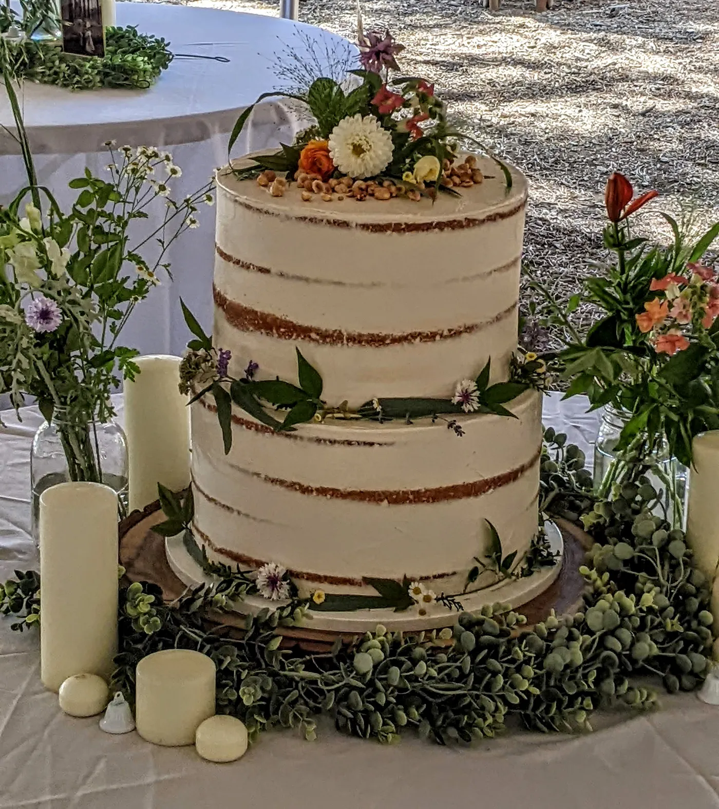 Two-tier semi-naked wedding cake with fresh flowers and hazelnuts, set among candles and greenery on a reception table
