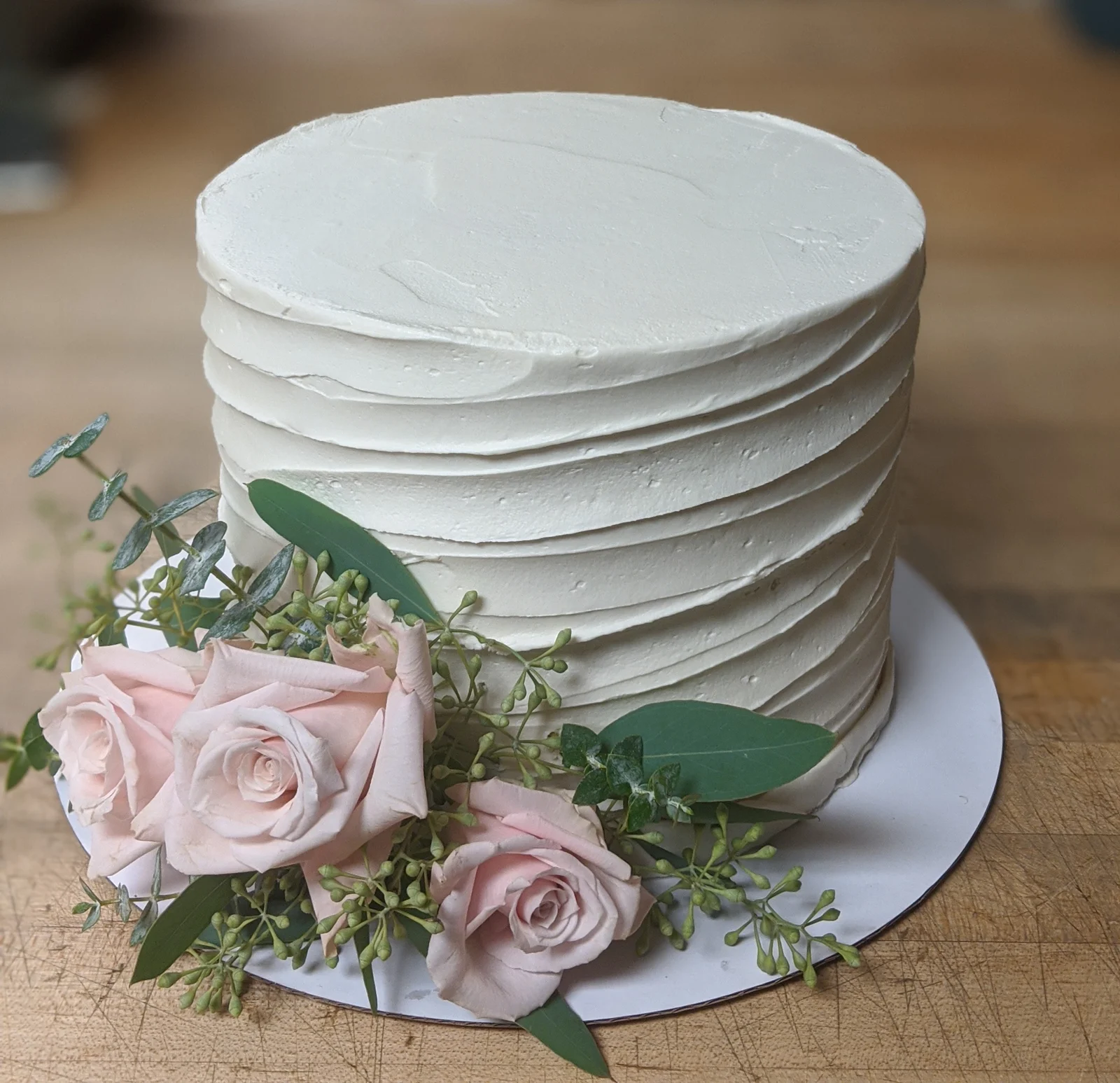 White ribbed buttercream cake with blush roses and seeded eucalyptus on a butcher block