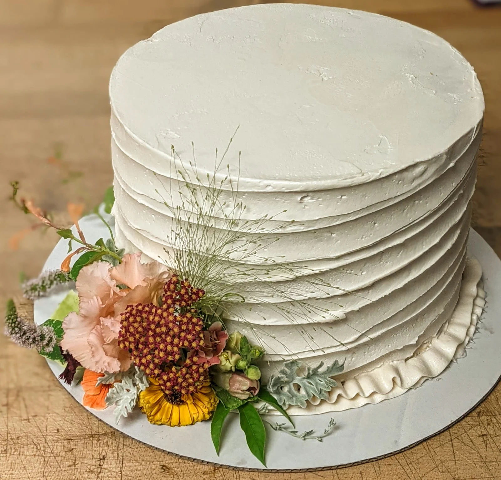 White ribbed buttercream cake with yarrow, marigold, dusty miller and a spray of dried grass
